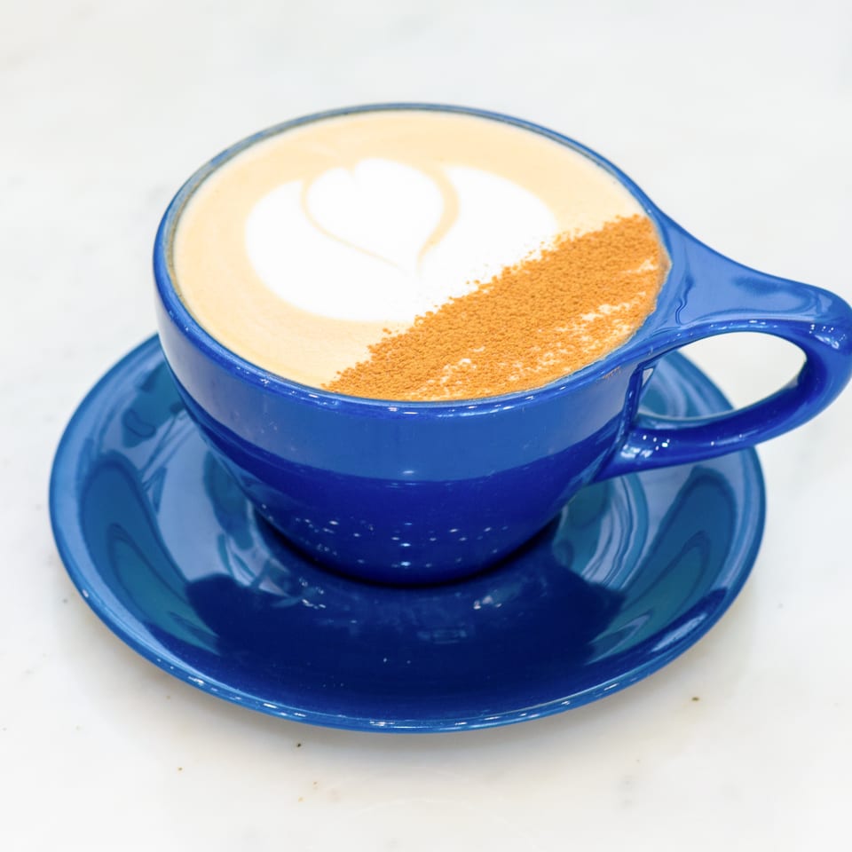 Creamy cappuccino topped with a heart-shaped foam design and cinnamon, served in a blue cup and saucer.