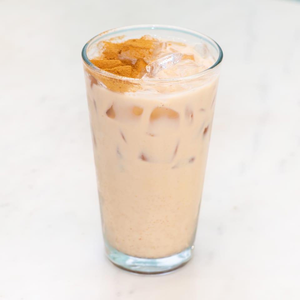 Creamy iced coffee in a clear glass, topped with whipped foam and cinnamon.