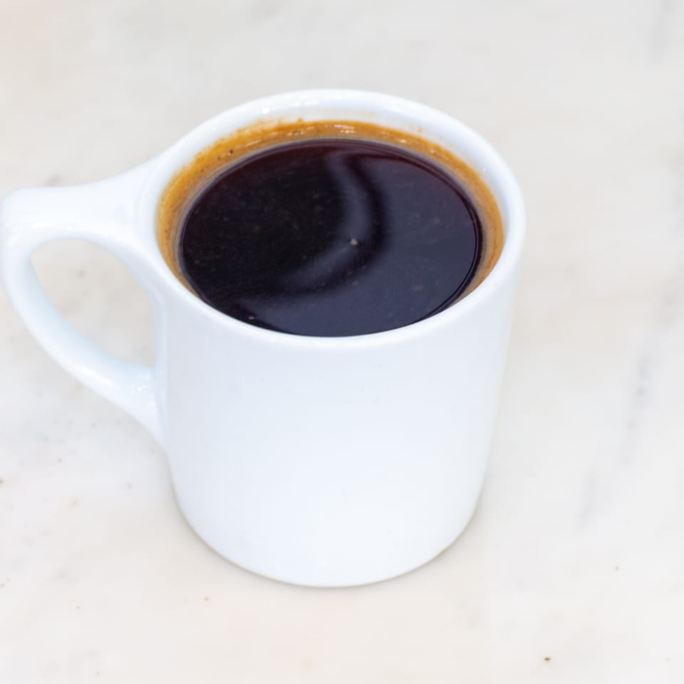 White ceramic cup filled with dark coffee on a light-colored tabletop.