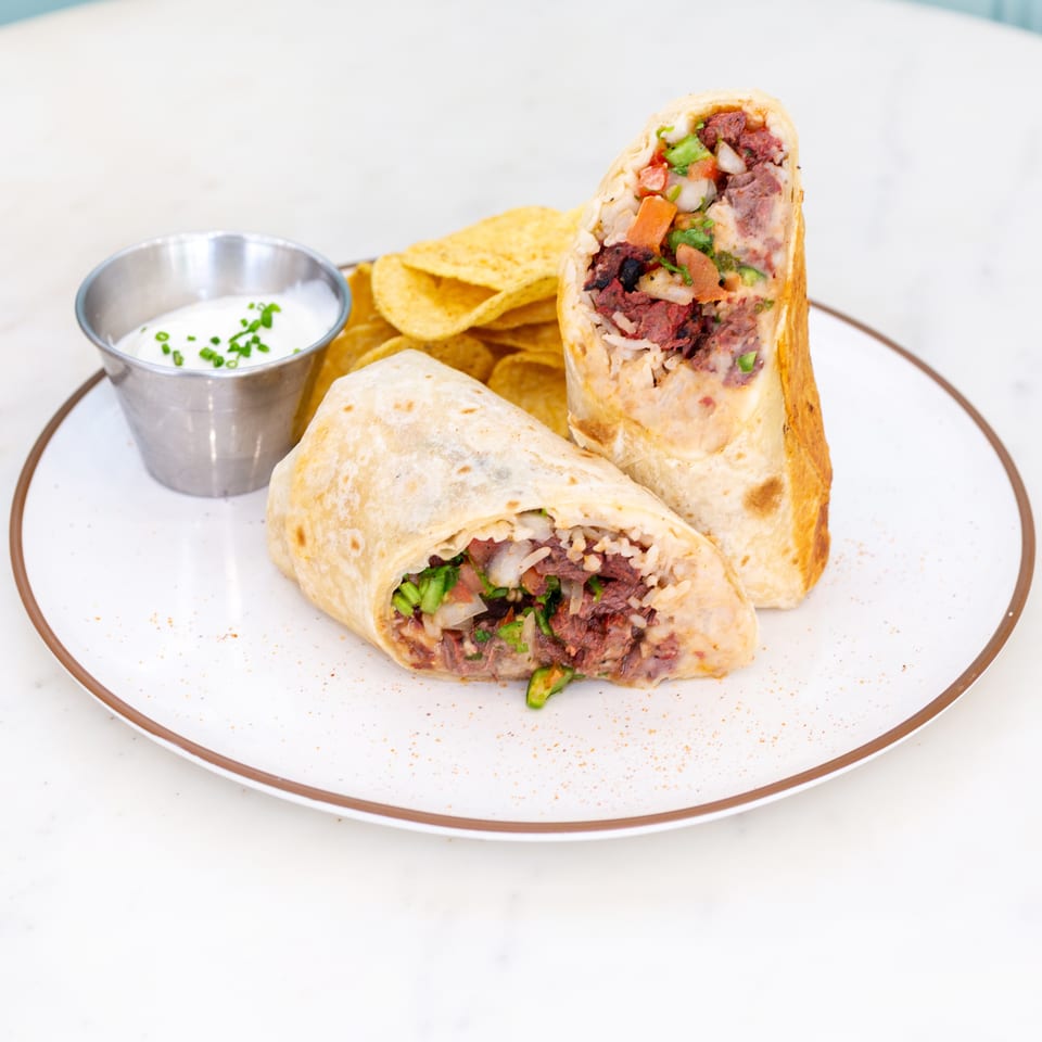 Two halves of a stuffed beef burrito with vegetables, tortilla chips, and sour cream on a plate.