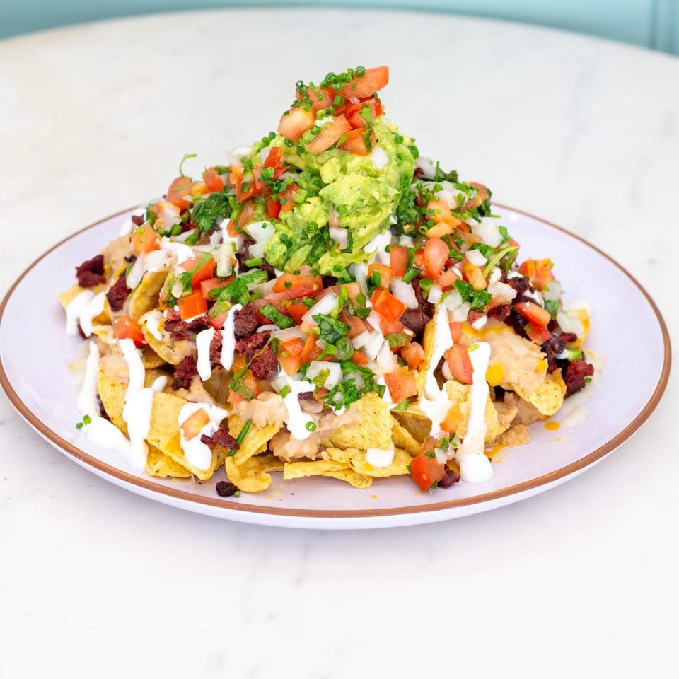 Loaded plate of nachos topped with beans, cheese, sour cream, pico de gallo, herbs, and a mound of guacamole.