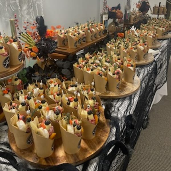 A buffet table with numerous individual charcuterie cups, decorated with Halloween-themed accents.