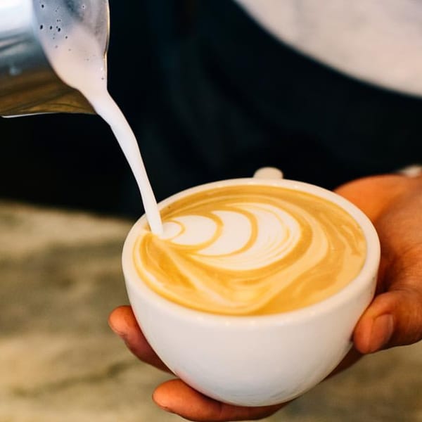 Barista pouring steamed milk into a white cup, creating latte art at Float Restaurant.