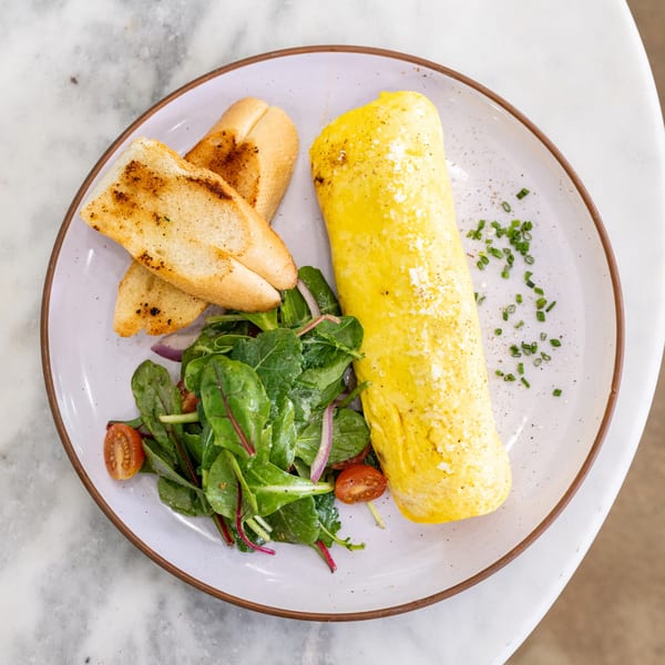 A rolled omelet with toasted bread, a green salad with cherry tomatoes, and chives on a plate.