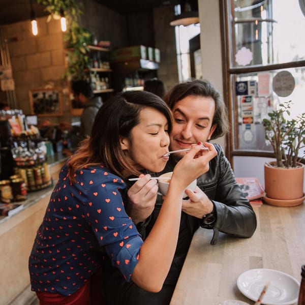 A couple sharing a drink at a cafe, the woman sips from a cup held by the man.