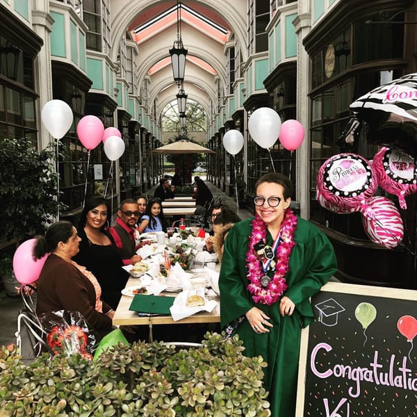 A graduate in a green gown and lei smiles with family at a celebratory meal at Float Restaurant.