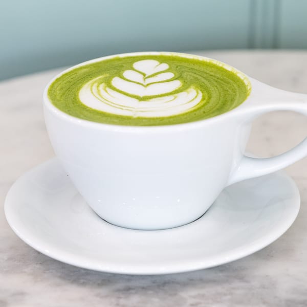 A vibrant green matcha latte with delicate white latte art in a white cup and saucer.