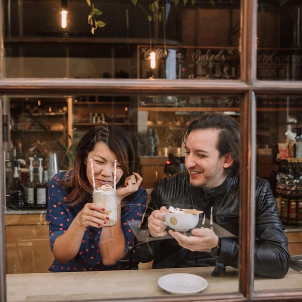 A smiling couple enjoying drinks at Float Restaurant, seen through a cafe window.